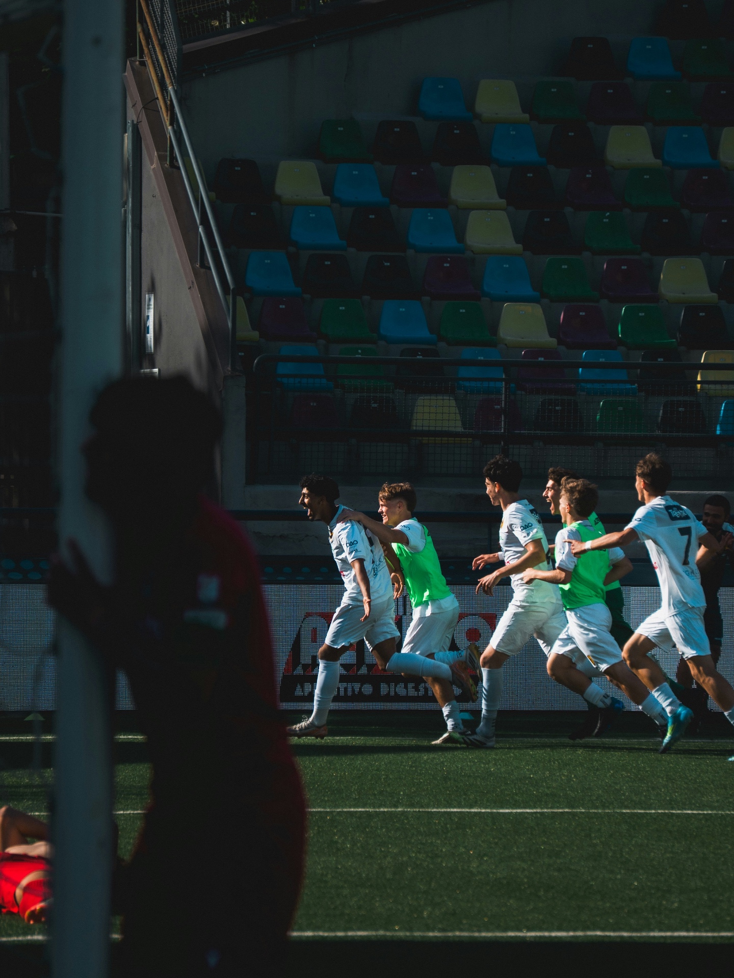 Players celebrating a goal as they run towards the sideline in a stadium